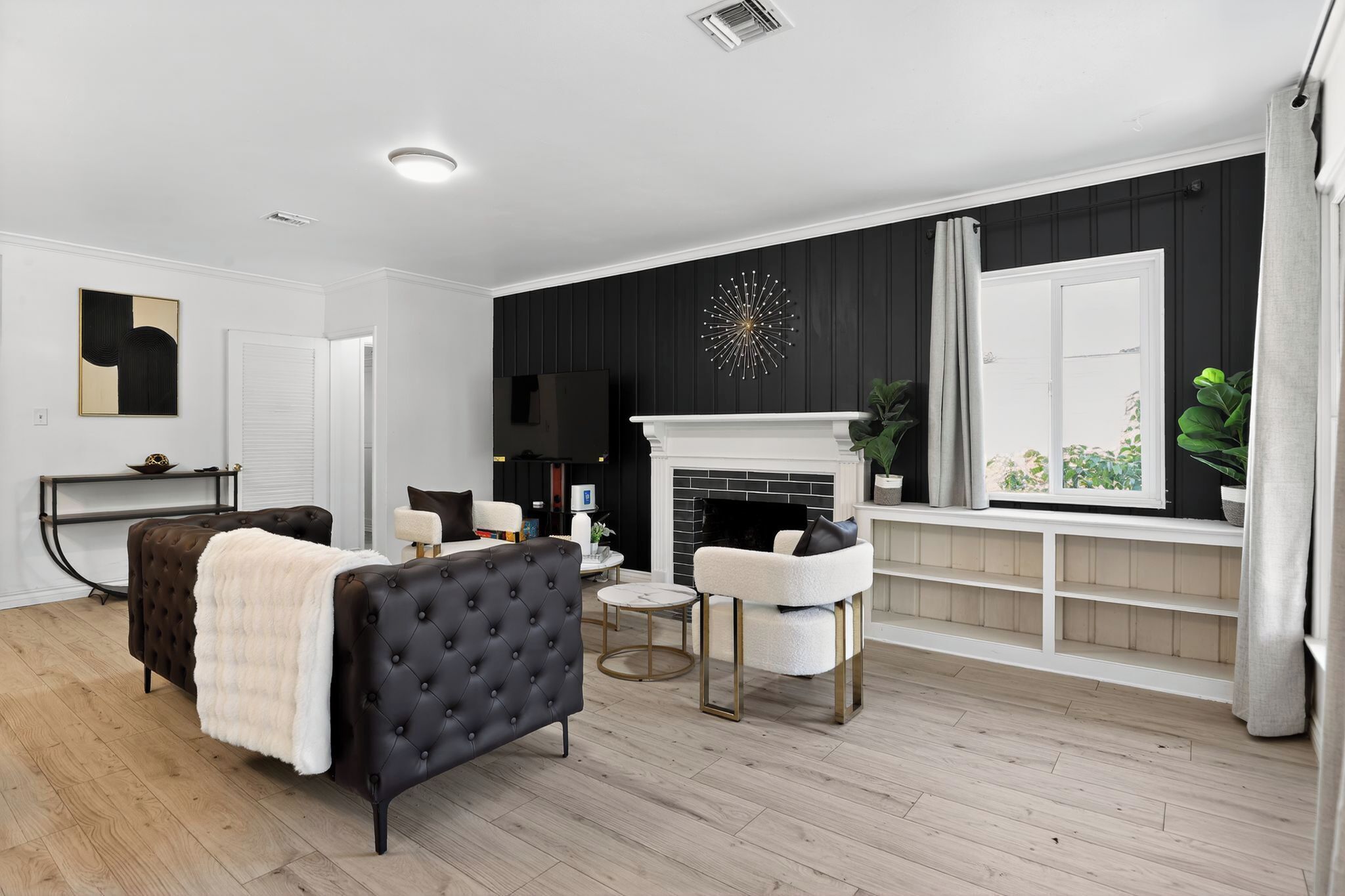 Un salon avec une cheminée, un canapé noir et blanc, une table basse ronde et un fauteuil blanc.