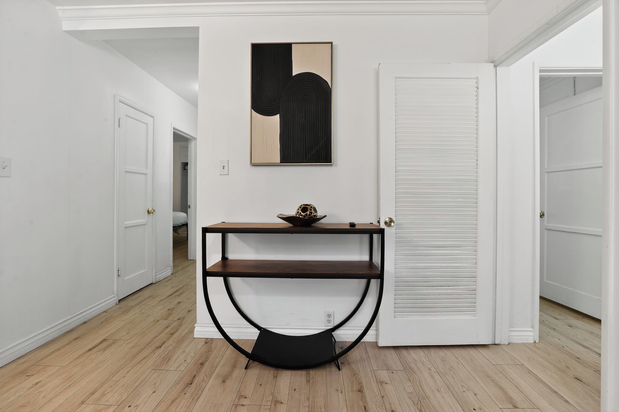 A hallway with a white door, a white wall, and a wooden floor.