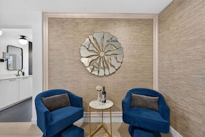 A modern interior with two blue armchairs, a small round table with a bottle and glass, and a decorative wall piece. - Wanderlust | Pool+Spa, Sunken BBQ, FirePit, Games! (Coachella)