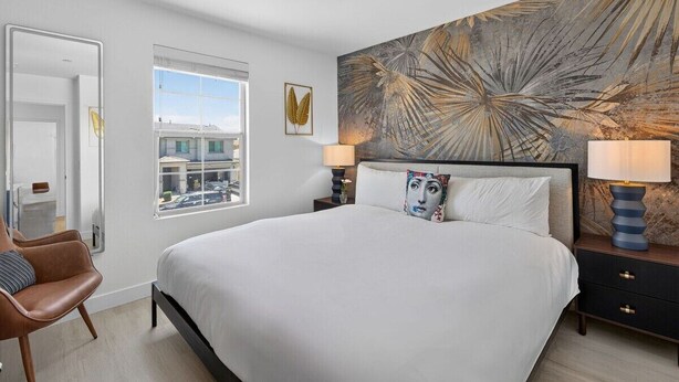 Ein modernes Hotelzimmer mit einem großen Bett, zwei Nachttischen, einem Fenster mit Blick und einem dekorativen Wandbild.