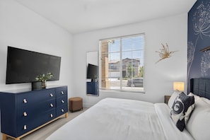 A bedroom with a bed, a dresser, a television, and a window with blinds. - Wanderlust | Pool+Spa, Sunken BBQ, FirePit, Games! (Coachella)