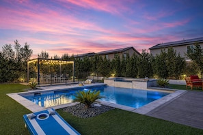 Uma piscina com espreguiçadeiras, área de estar coberta e vista para casas ao fundo.