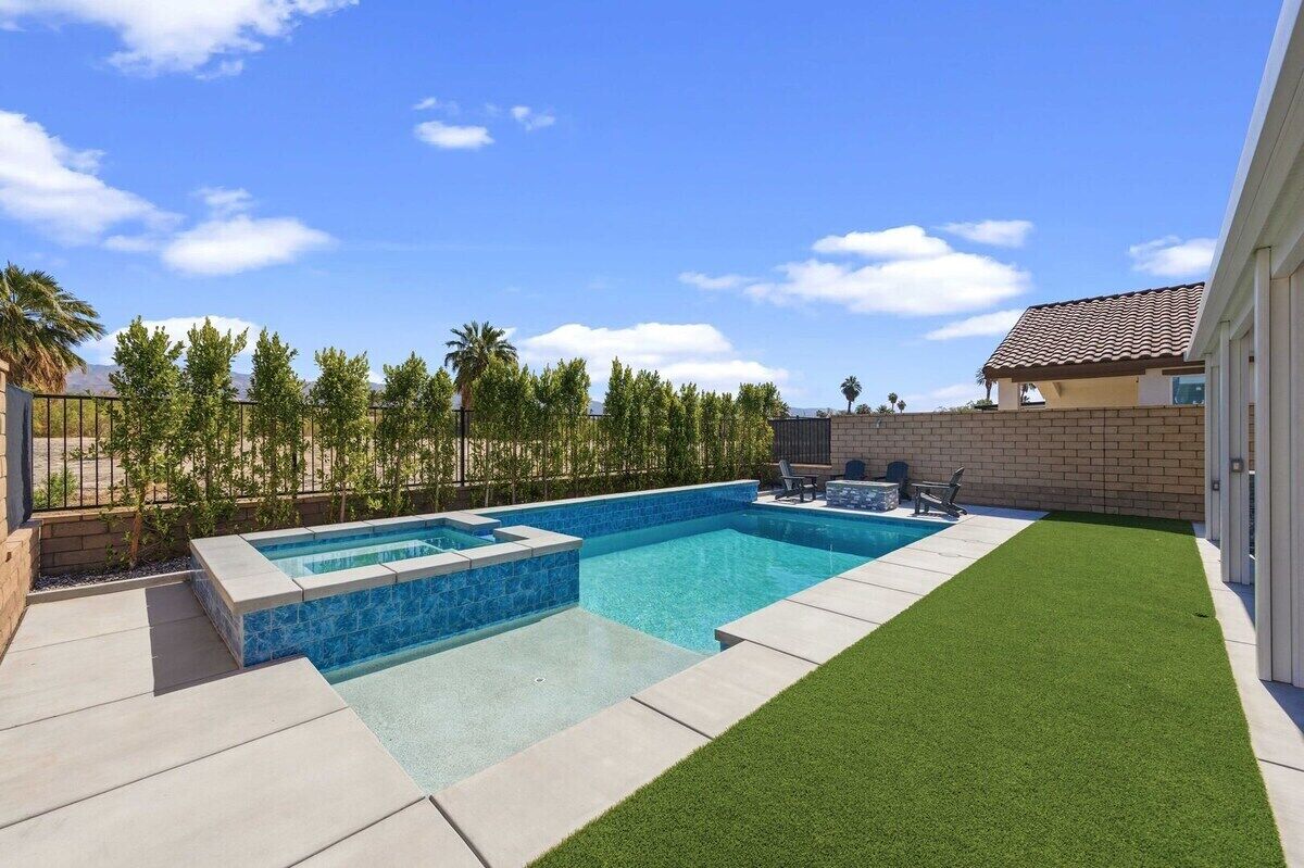 Una piscina rectangular con borde de azulejos, rodeada por un deck de concreto y una sección de césped artificial.