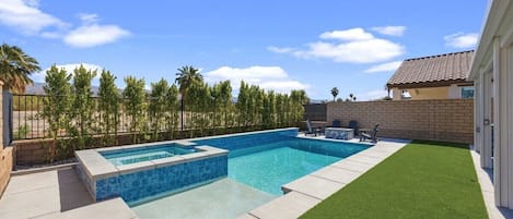 Una piscina rectangular con borde de azulejos, rodeada por un deck de concreto y una sección de césped artificial.