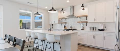 A modern kitchen with a central island, bar stools, and white cabinetry.