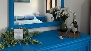 A blue dresser with a mirror, a vase with flowers, and two glasses on a placemat. - Vacation home Annameri (Terrasini)