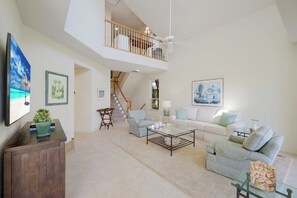 A spacious living room with a high ceiling, a staircase, a balcony, and a large painting on the wall. - Boca Bay Kentia - 3 bed / 3 bath - 30 night minimum - Summer/Fall Pricing! (Boca Grande)