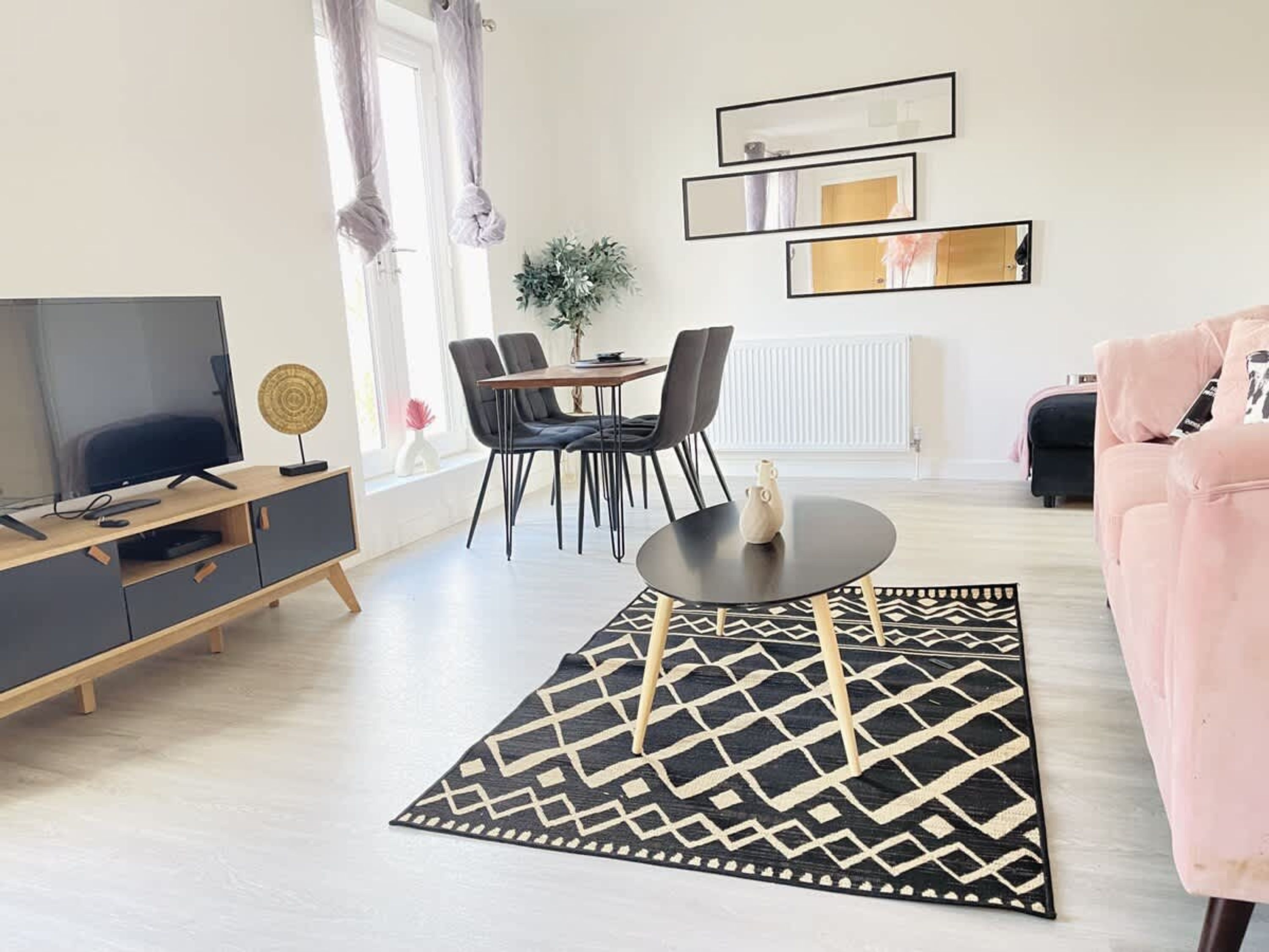 A modern living room with a TV, dining table, chairs, and a pink sofa.