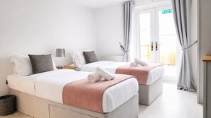 A hotel room with two beds, a lamp, a radiator, and a view of the outside. - Amythest 4BR all With Ensuite Parking (Cambridge)