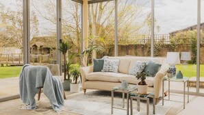 Ein modernes Wohnzimmer mit großen Fenstern, einem beigen Sofa, einem Couchtisch und einem kleinen Beistelltisch.