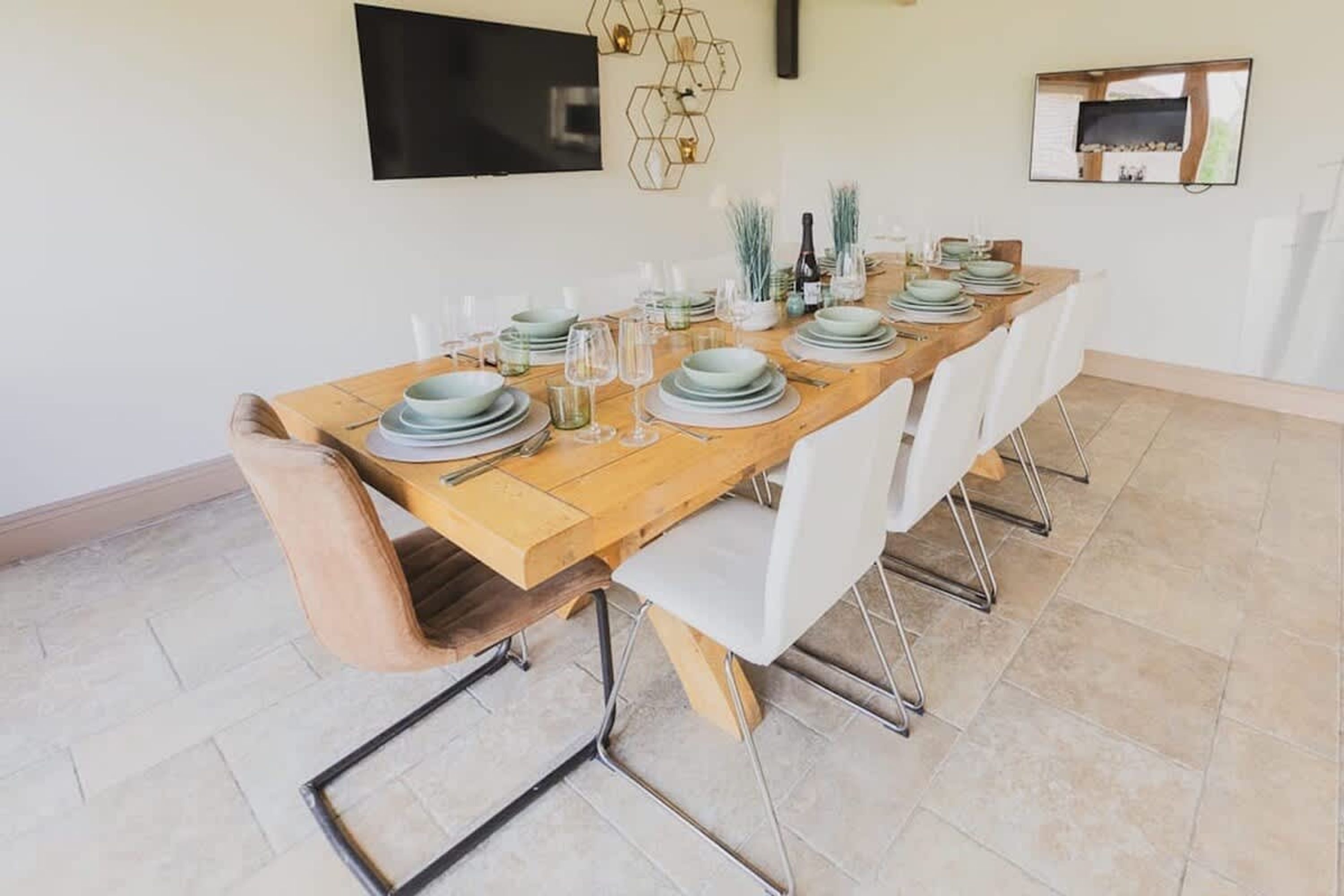 A dining area with a wooden table set for six, white chairs, a flat-screen TV, and a decorative wall piece.