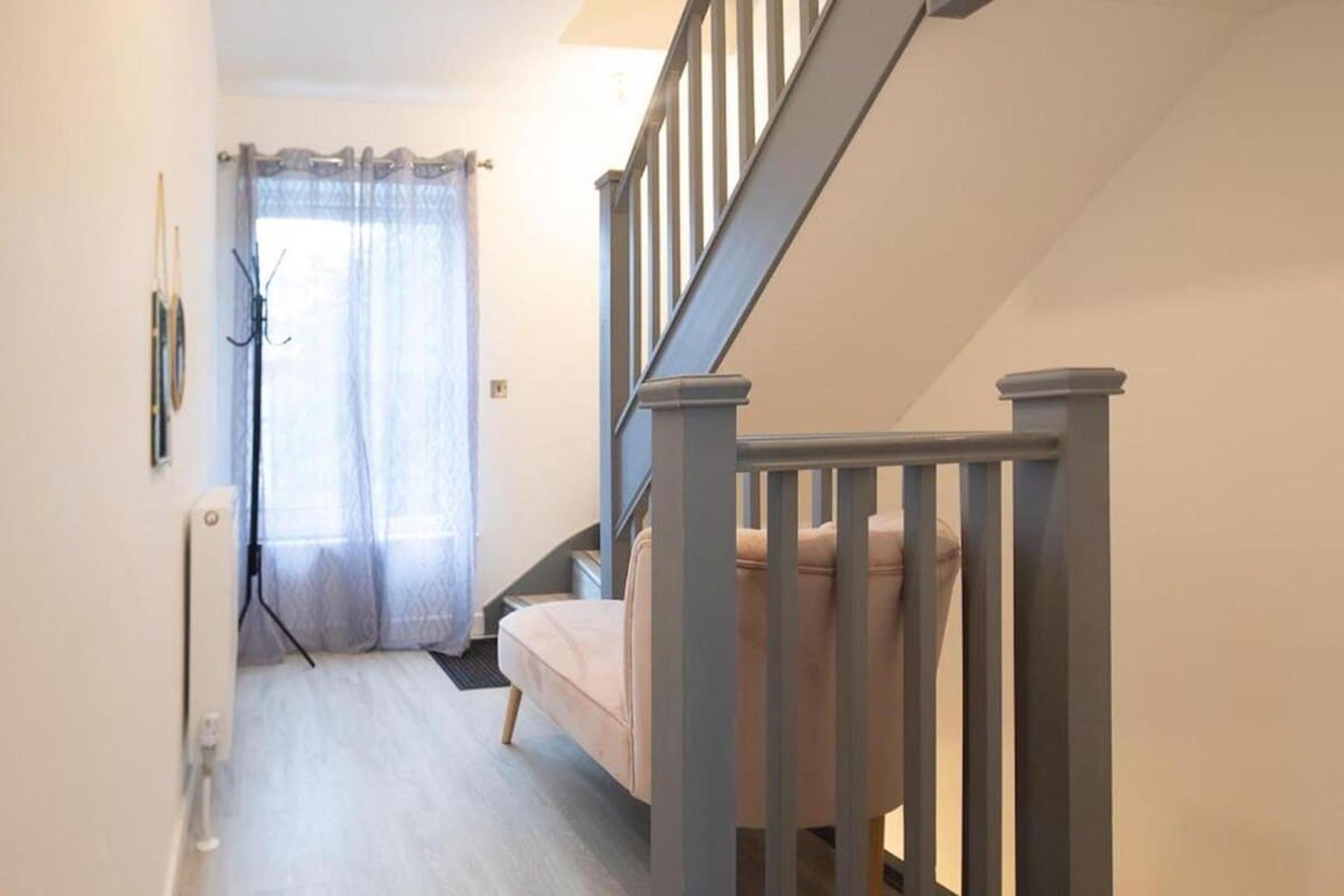 A staircase with a handrail, a light-colored wall, a door with a curtain, and a radiator.