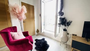 Una sala de estar moderna con una silla roja, un manto mullido negro, un ventanal con cortinas y una planta.