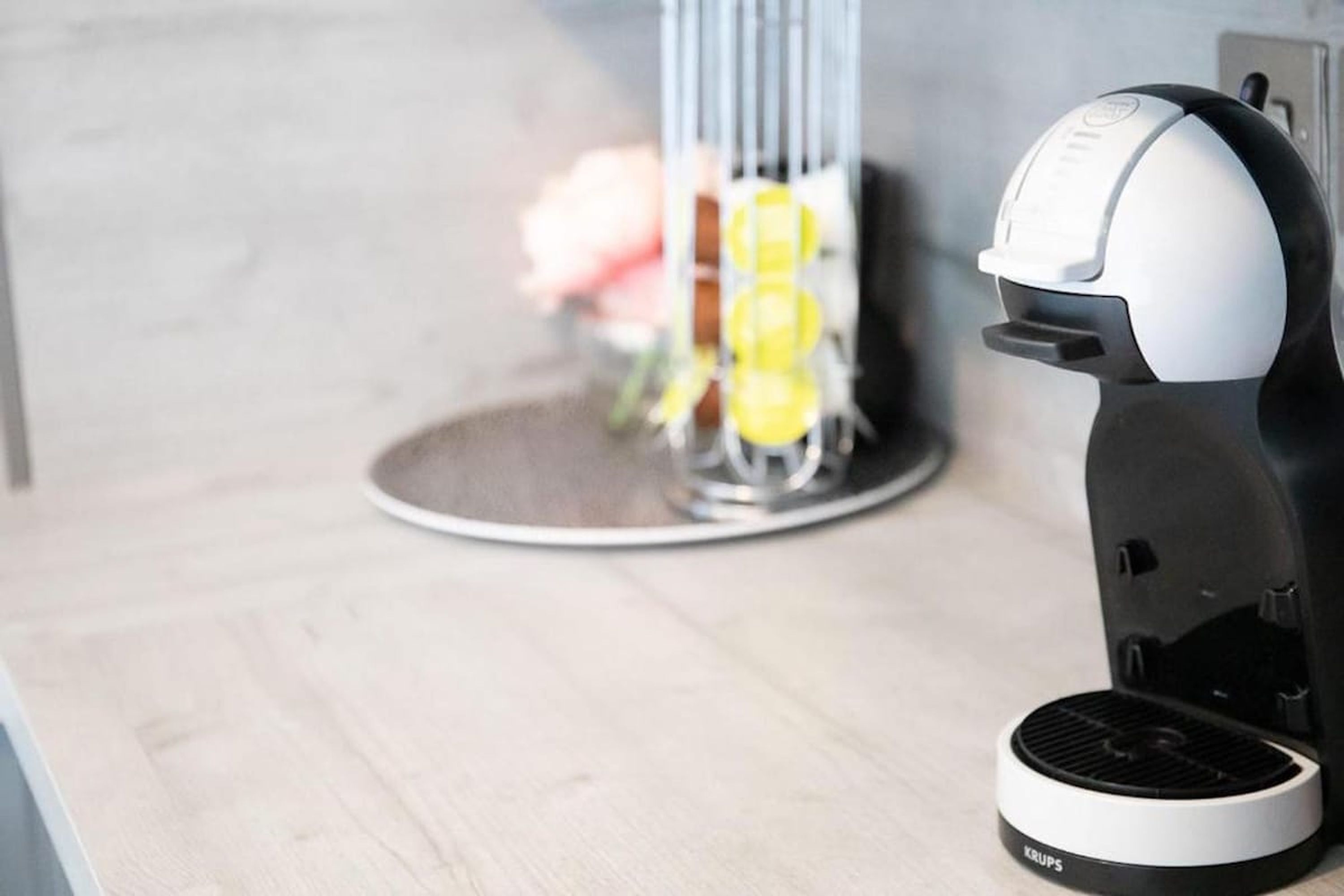 A coffee machine on a table with a flower vase in the background.