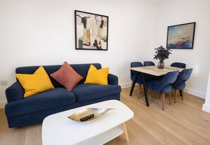 A modern living room with a blue sofa, a white coffee table, and a dining area with a wooden table and blue chairs.