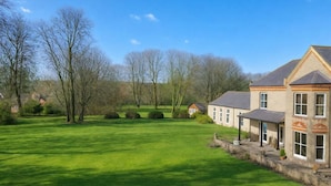 A large, open grassy area with a building featuring a stone facade and multiple windows. - 2 BR Sofabed 11 Mins to Gallops Parking Garden (Newmarket)