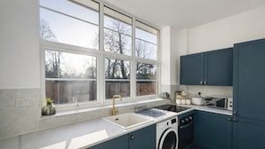 A modern kitchen with a large window, a washing machine, and blue cabinets. - 2 BR Sofabed 11 Mins to Gallops Parking Garden (Newmarket)