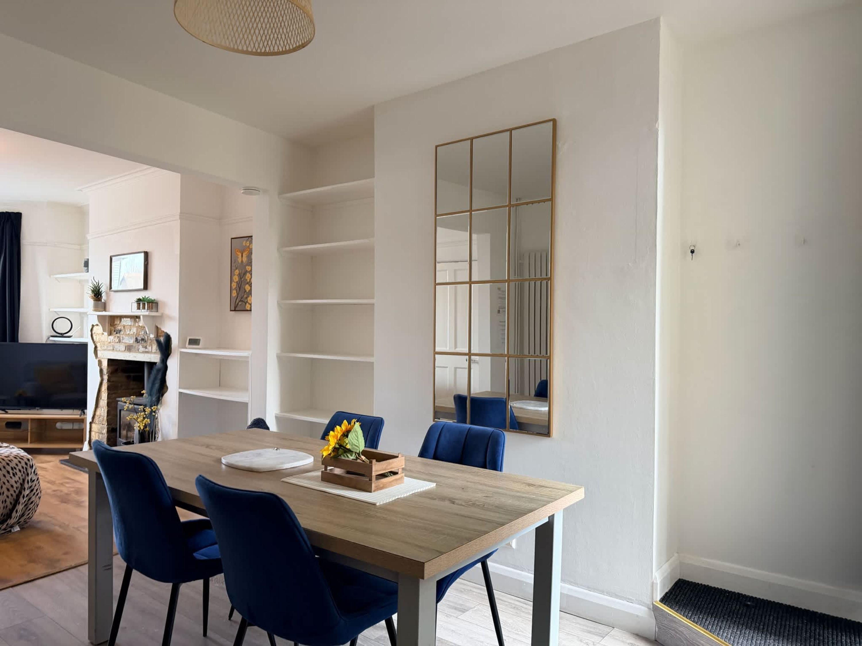 Un salon moderne avec une table à manger en bois, des chaises bleues, un grand miroir et des étagères intégrées.