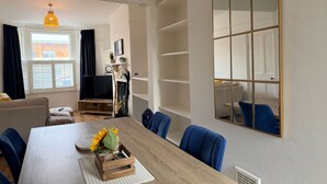 A modern living room with a wooden dining table, blue chairs, a TV, and a large mirror.