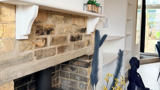 A fireplace with a brick surround, a black wood stove, and decorative items including a plant, a painting, and feather-like decorations.