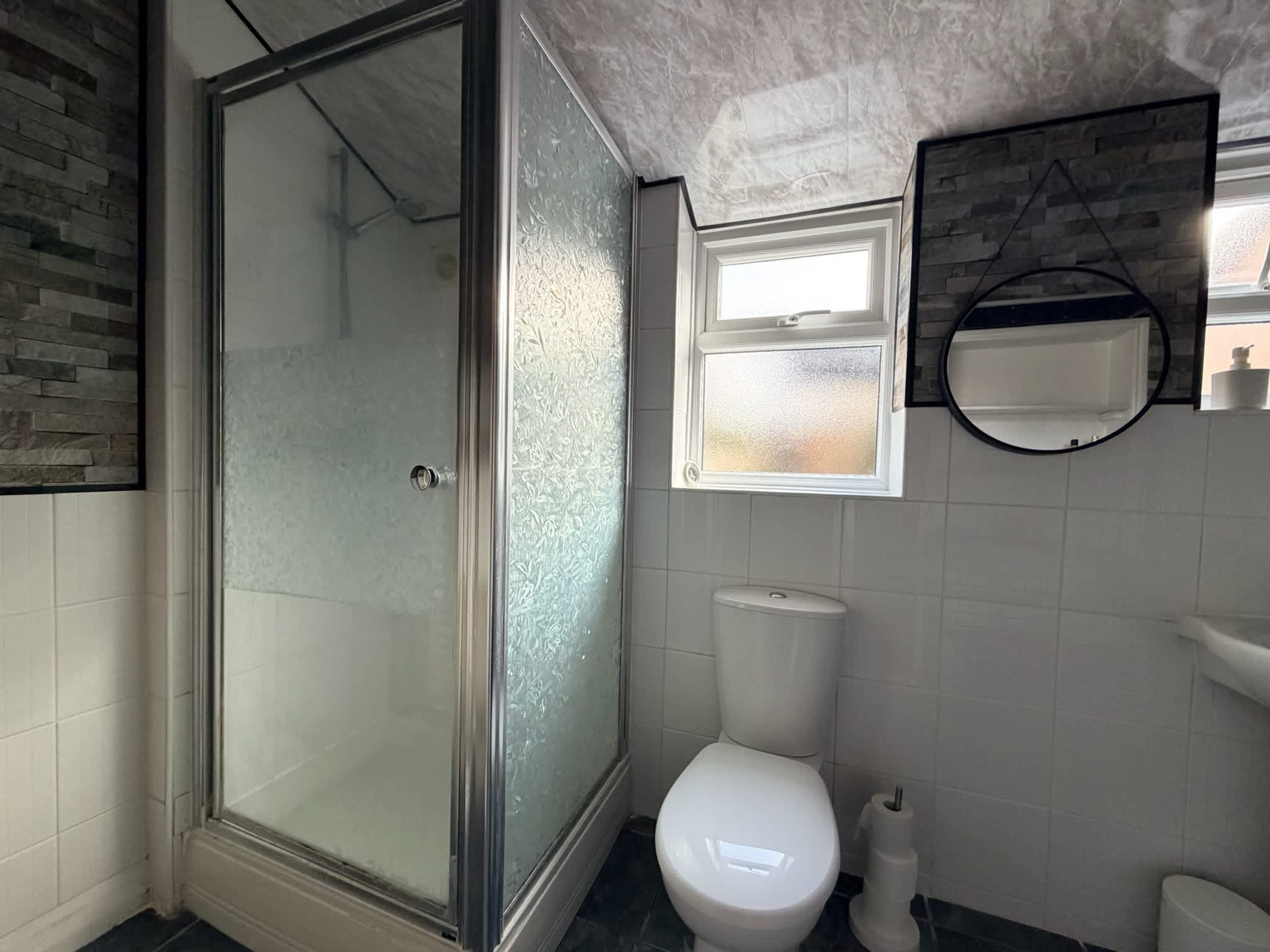 A bathroom with a glass shower enclosure, a toilet, a sink, and a window.