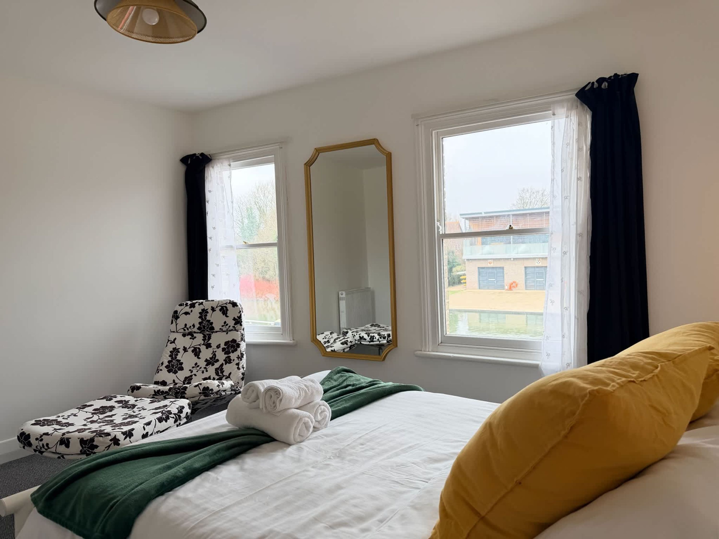Ett hotellrum med en säng, en stol, en spegel och fönster med gardiner.