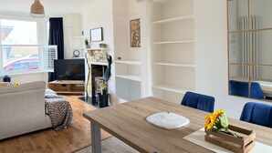 A modern living room with a sofa, a dining table, a fireplace, and a large mirror.