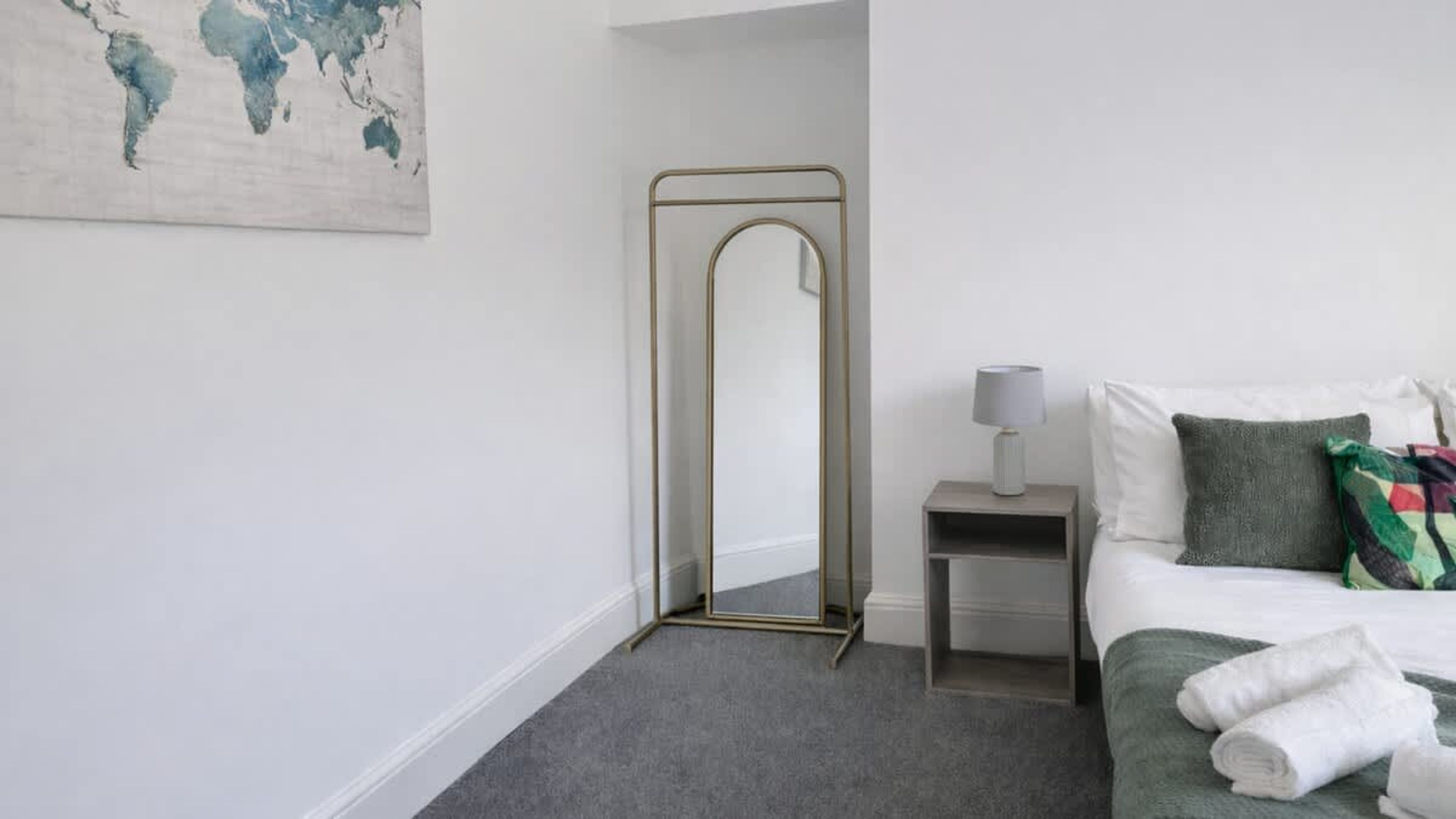 A bedroom with a bed, a nightstand with a lamp, a mirror, and a world map on the wall.