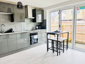 Una cocina moderna con horno empotrado, un lavamanos y una zona de comedor con mesa y sillas.