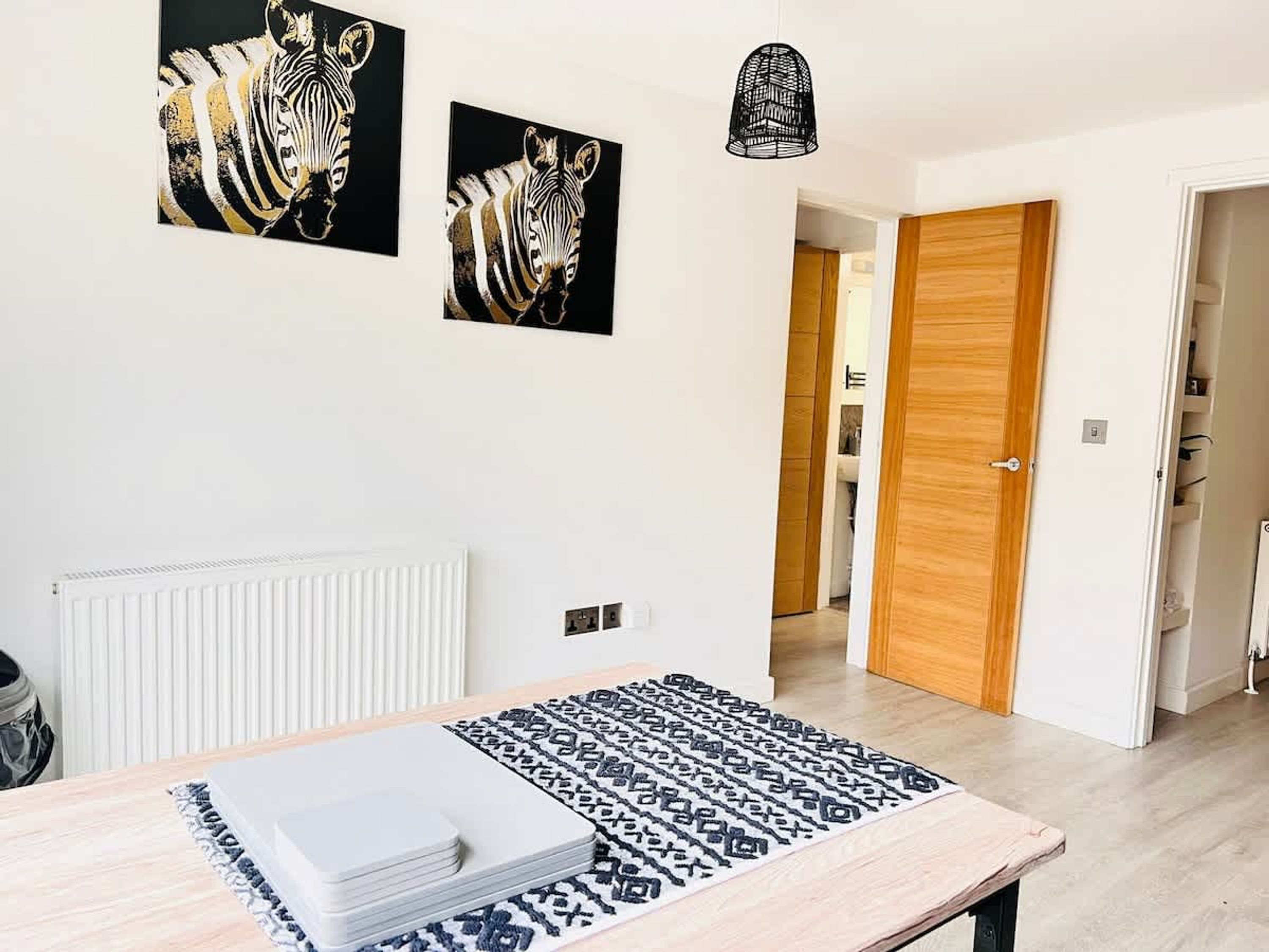A modern room with a dining table, two zebra paintings, a patterned rug, and a wooden door.