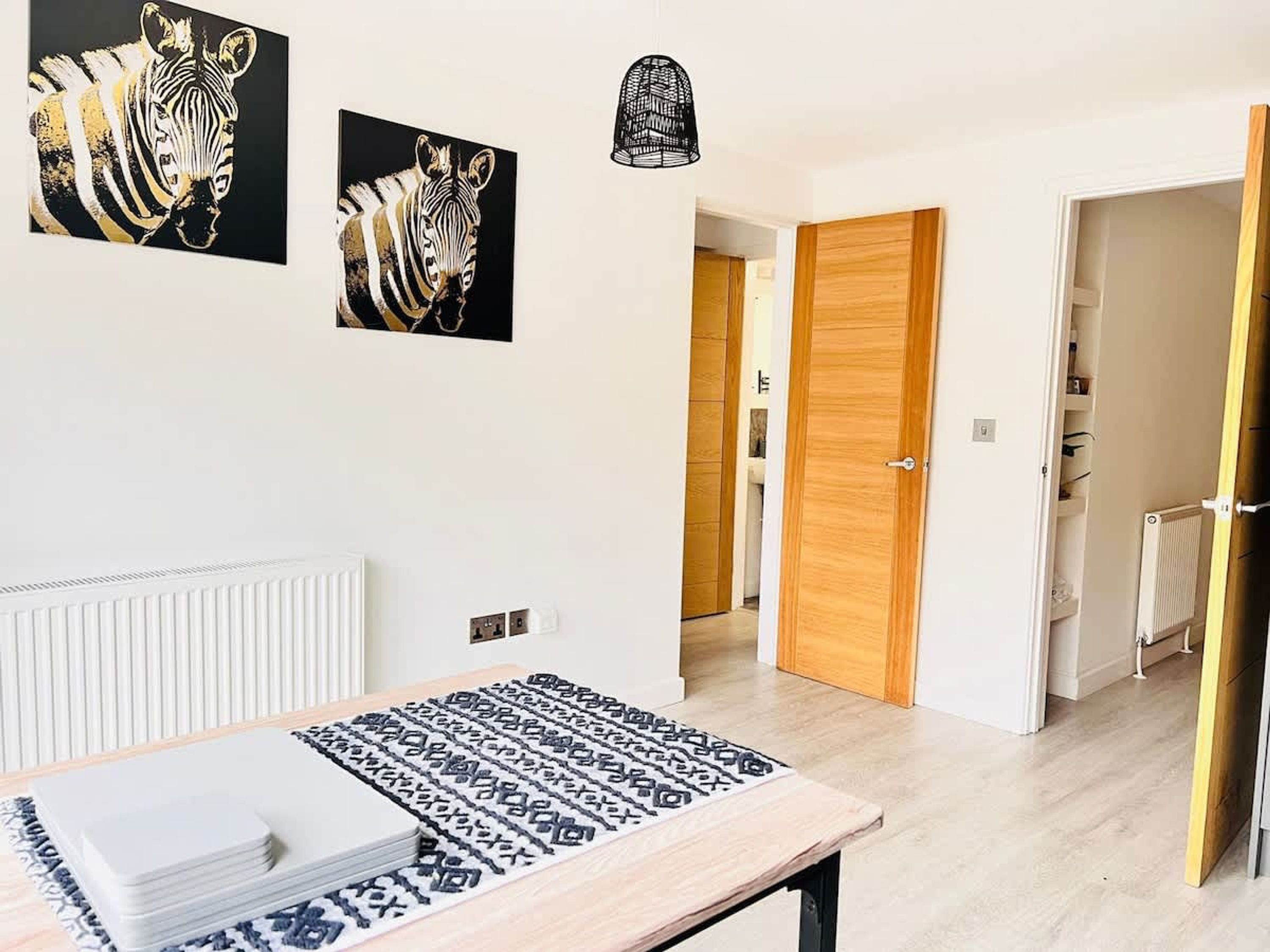 A modern room with a wooden table, two zebra-themed wall art pieces, a patterned rug, and a wooden door leading to another room.