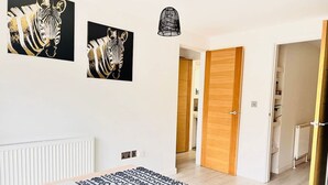 A modern room with a wooden table, two zebra-themed wall art pieces, a patterned rug, and a wooden door leading to another room. - Tanzanite Ground Floor 2BR Apart Pet Friendly (Cambridge)