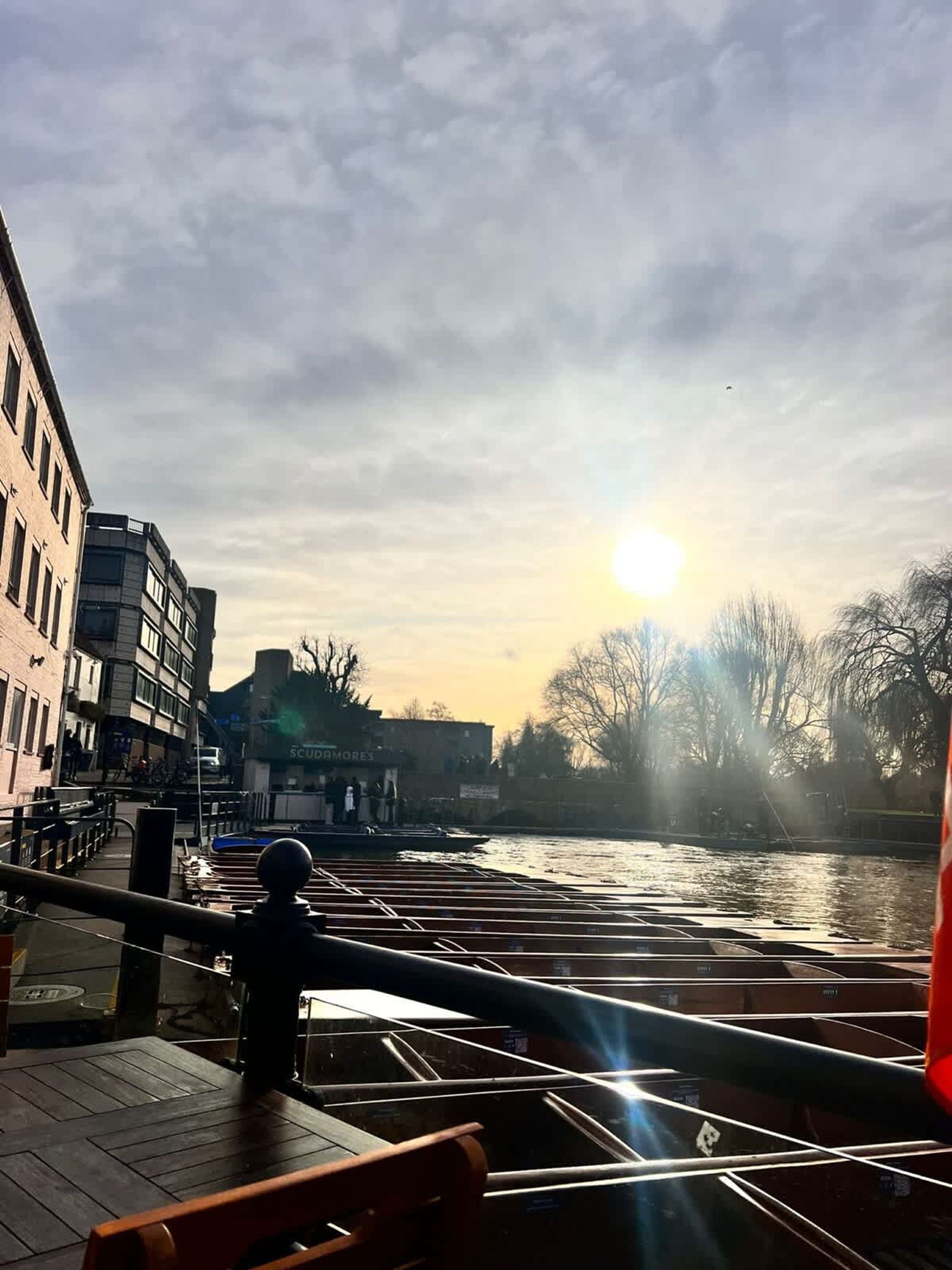 Vista del río con barcos amarrados, un puente y edificios al fondo.