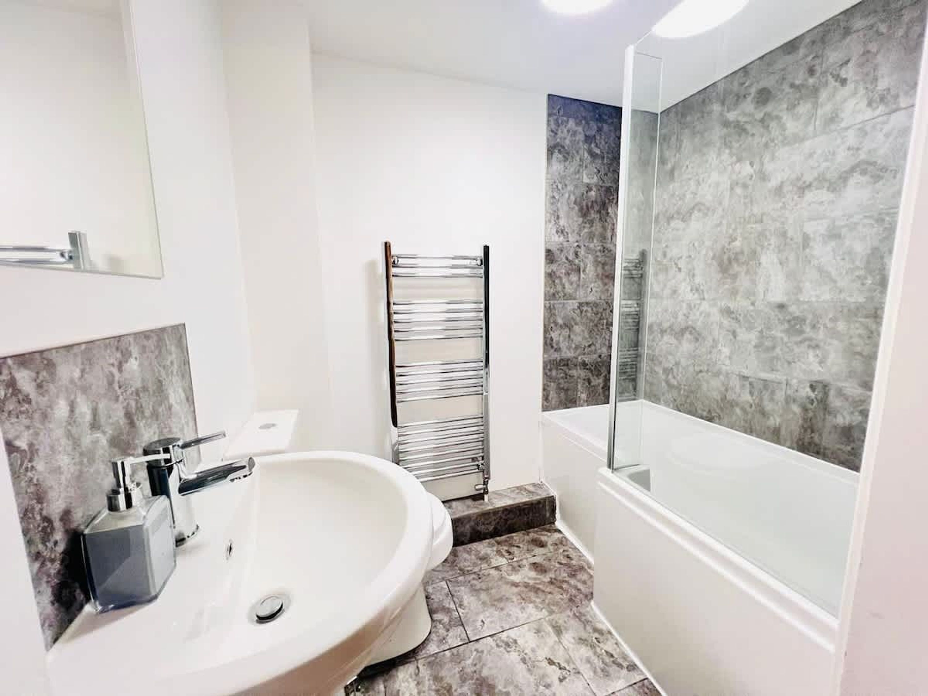 Une salle de bain avec un lavabo blanc, une cabine de douche en verre et un porte-serviettes.