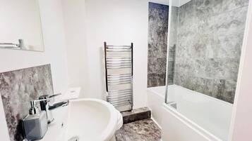 Une salle de bain avec un lavabo blanc, une cabine de douche en verre et un porte-serviettes.