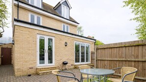 A two-story house with a brick exterior, large windows, and a patio with wicker furniture. - Tanzanite Ground Floor 2BR Apart Pet Friendly (Cambridge)