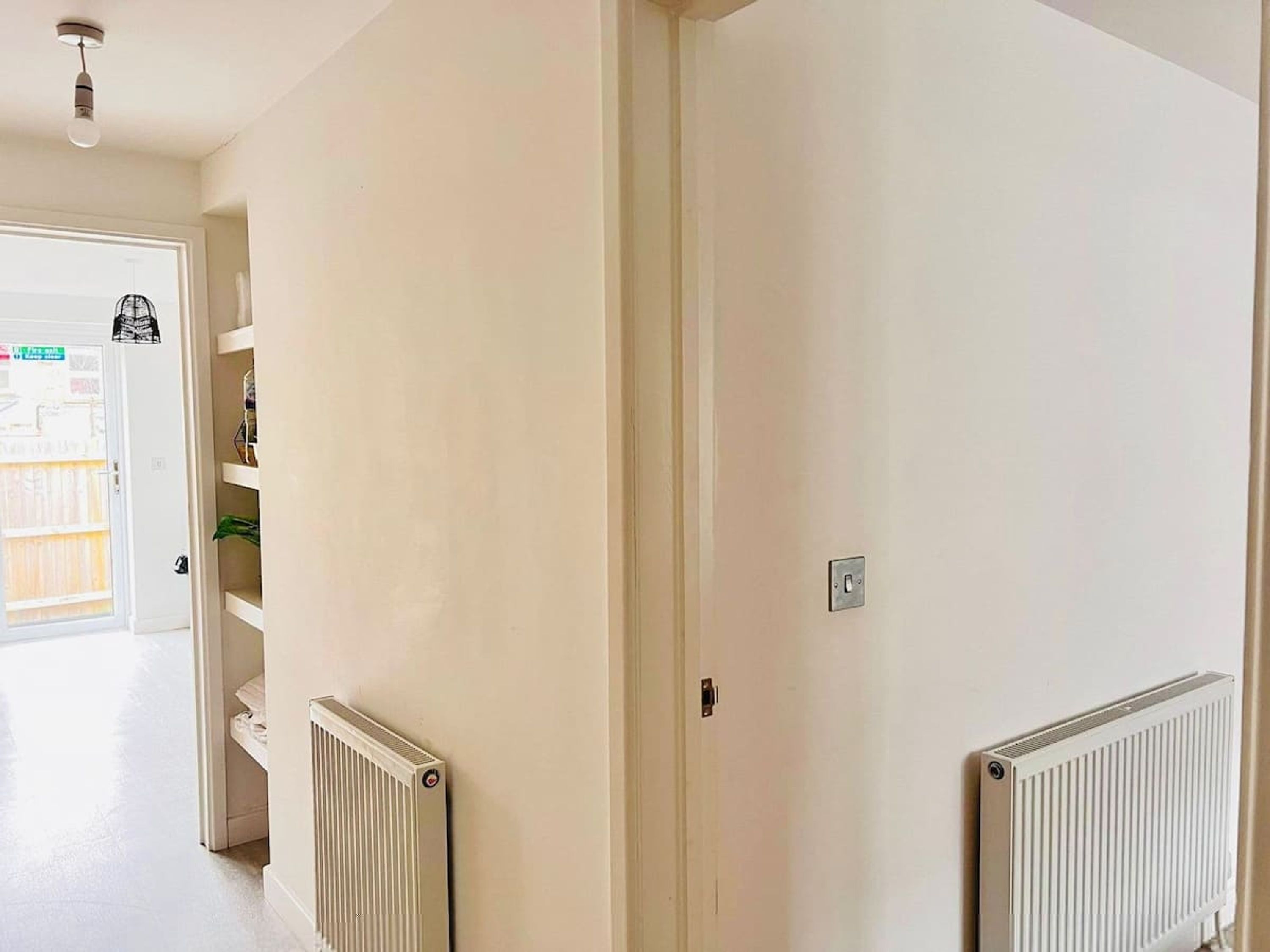 Un couloir aux murs blancs, avec un radiateur et une porte donnant sur une autre pièce.