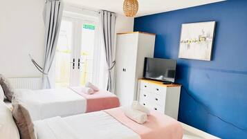 A bedroom with two beds, a TV on a dresser, and a painting on the wall.