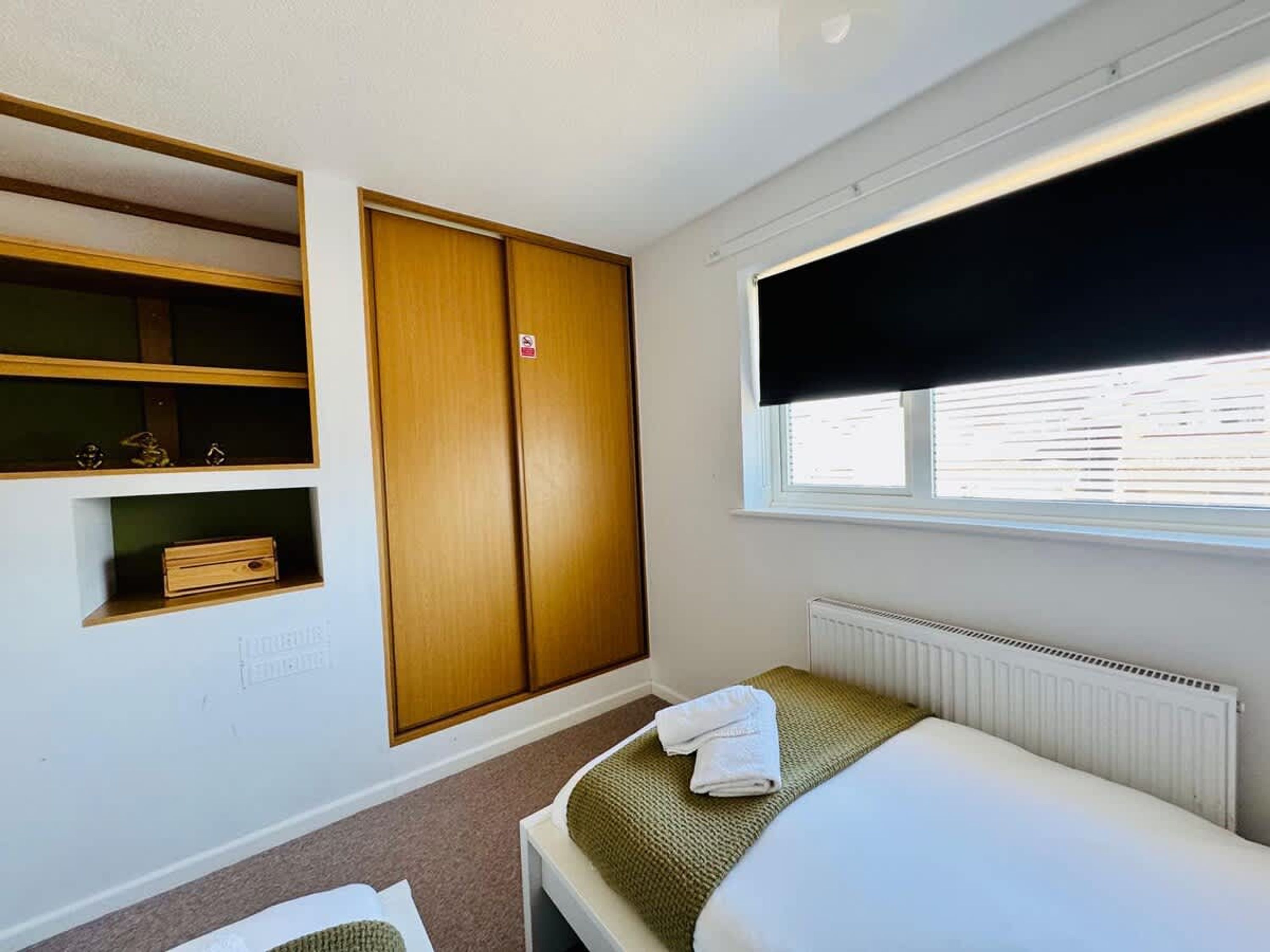 Een slaapkamer met een bed, een kledingkast, een plankunit en een raam met zonwering.