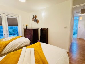 Ein Schlafzimmer mit zwei Betten, einem Schminktisch, einer Wanddekoration und Blick durch eine Schiebetür.