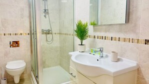 Un bagno moderno con doccia vetro, un water, un mobile lavabo con lavandino e una piccola pianta in vaso.