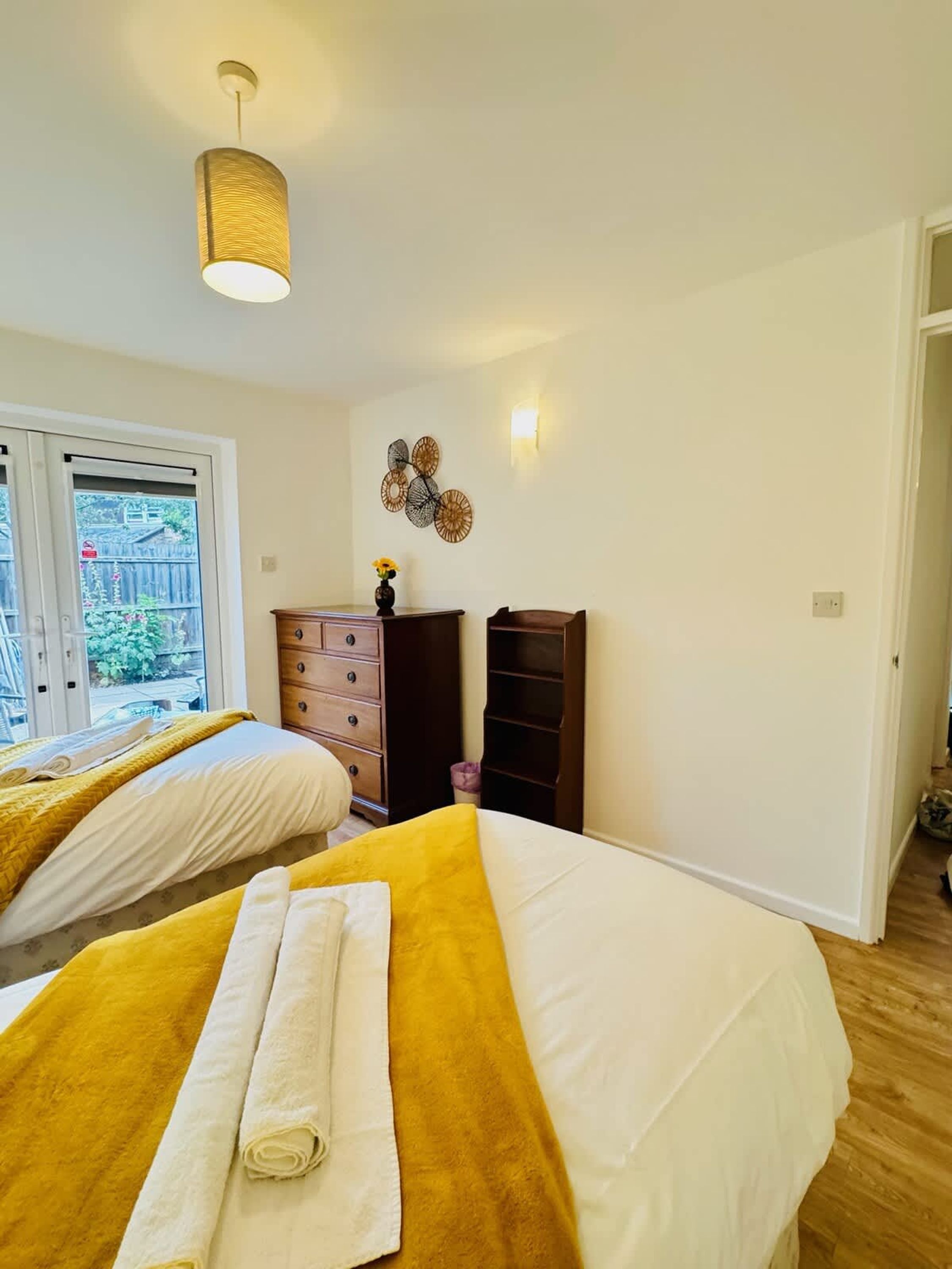 A bedroom with two beds, a window, a wall-mounted light, and a decorative wall piece.