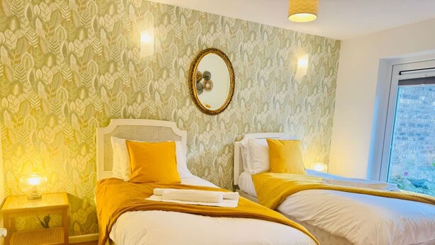 Camera d'albergo con due letti, uno specchio, una finestra e carta da parati decorata.