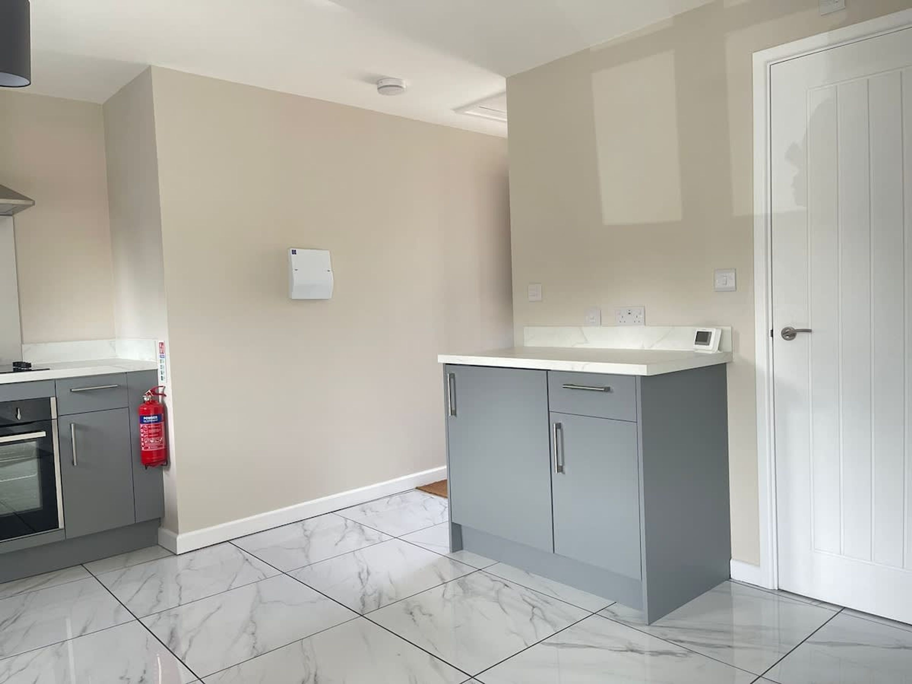 A kitchen with grey cabinets, a white countertop, and a fire extinguisher.
