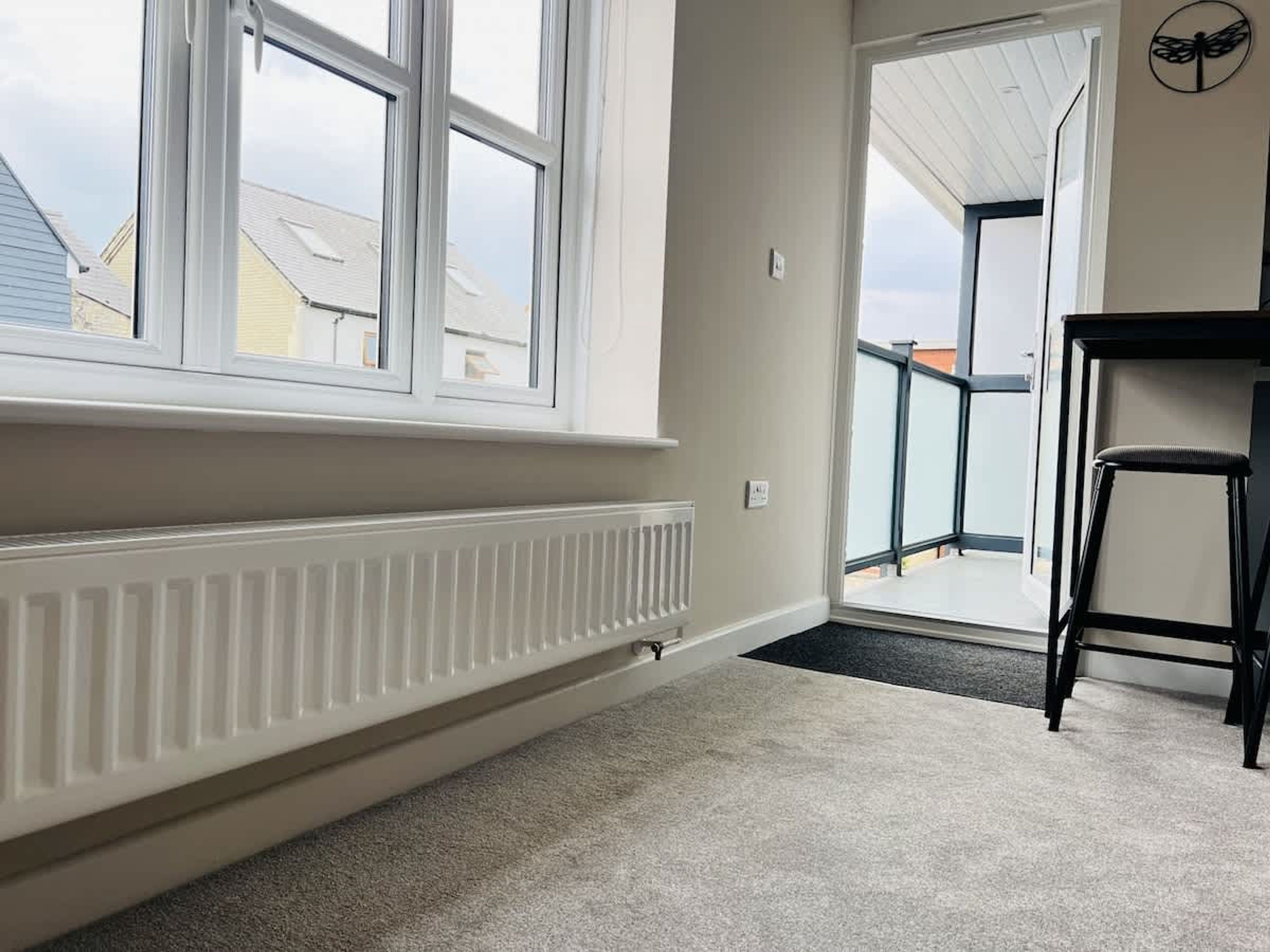 Una habitación con ventanas grandes, un radiador, una puerta que da al exterior y una silla.
