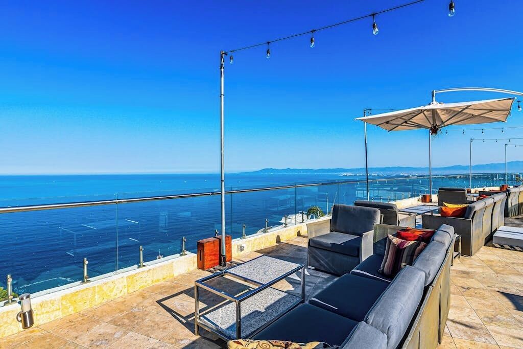 Une terrasse sur le toit avec des sièges extérieurs, une balustrade en verre et une vue sur la mer.