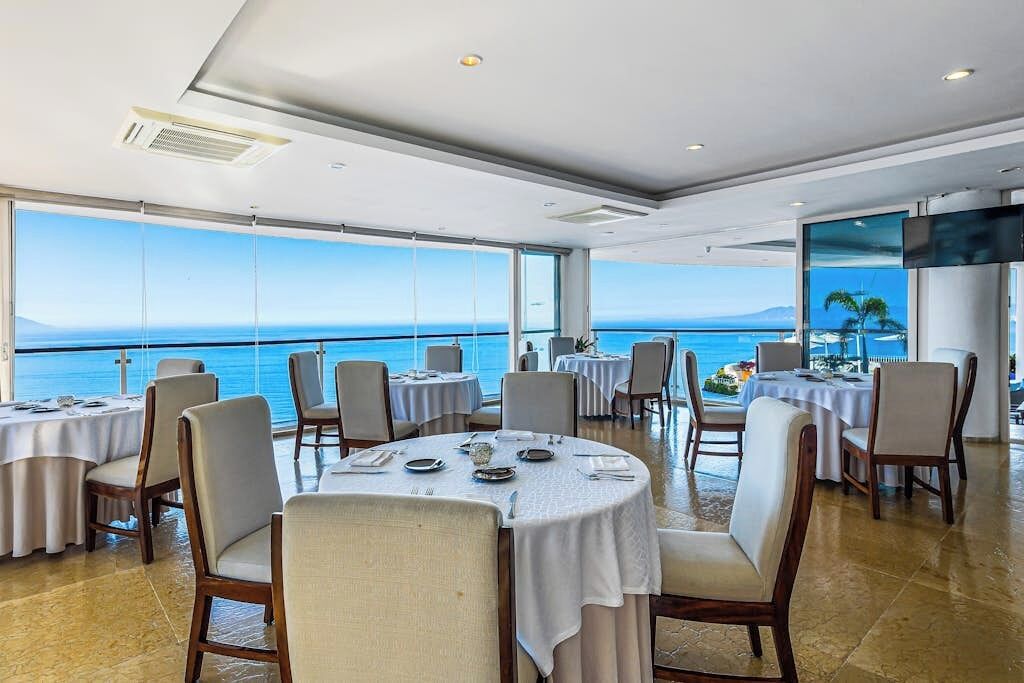 Un restaurant avec des tables et des chaises rondes, et une vue sur la mer.