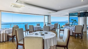 Ein Restaurant mit runden Tischen, Stühlen und Meerblick.