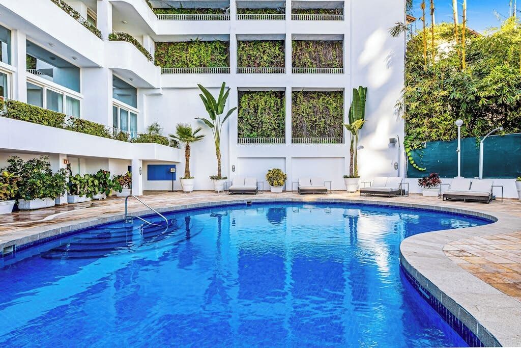 A modern hotel with a swimming pool, white balconies, and lush greenery.