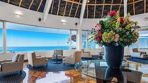 Eine geräumige Lobby mit einem großen Glastisch, bequemen Sitzgelegenheiten und Blick auf den Ozean.